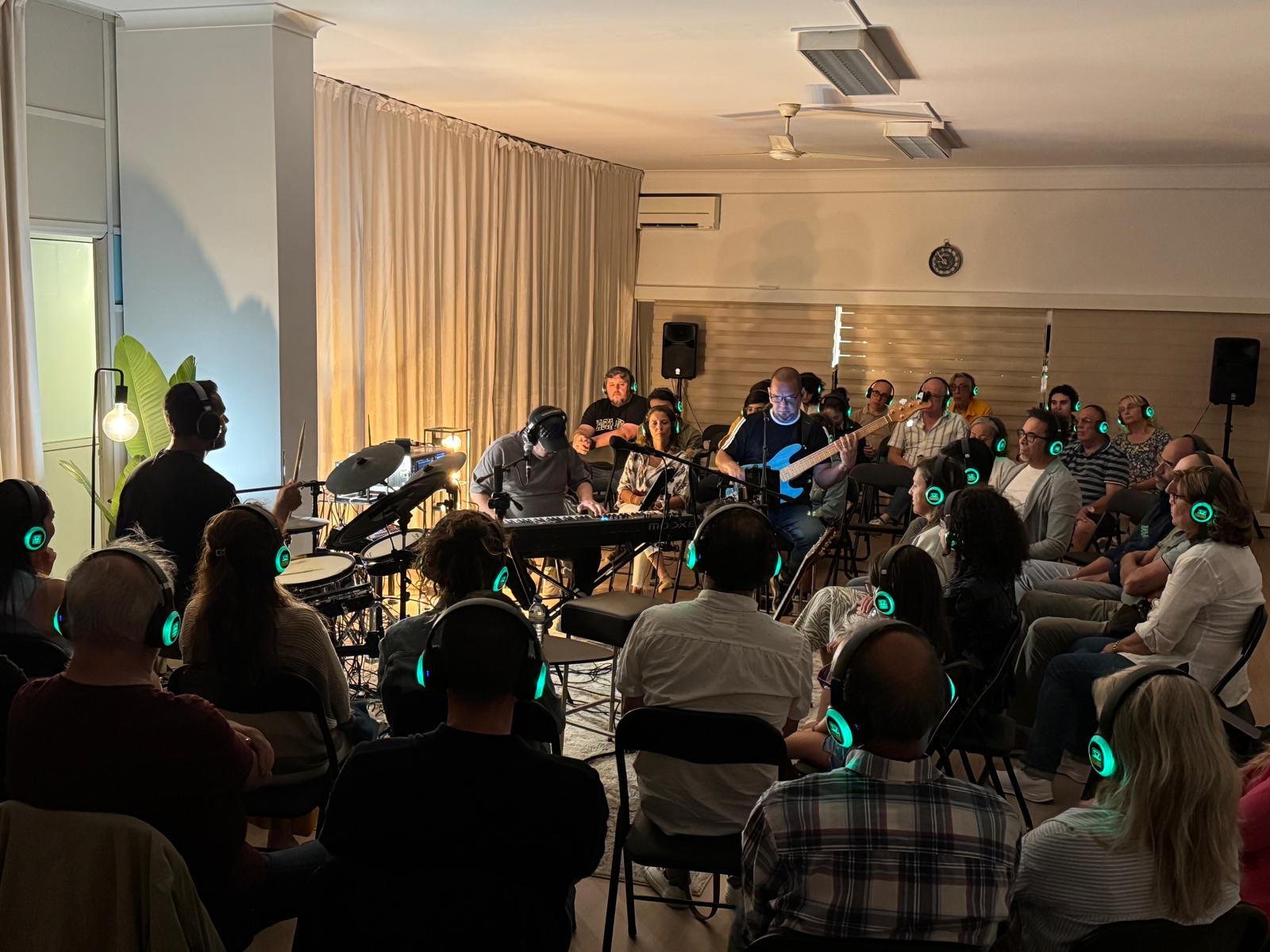 Músicos atuam no centro da sala rodeados pelo público com auscultadores